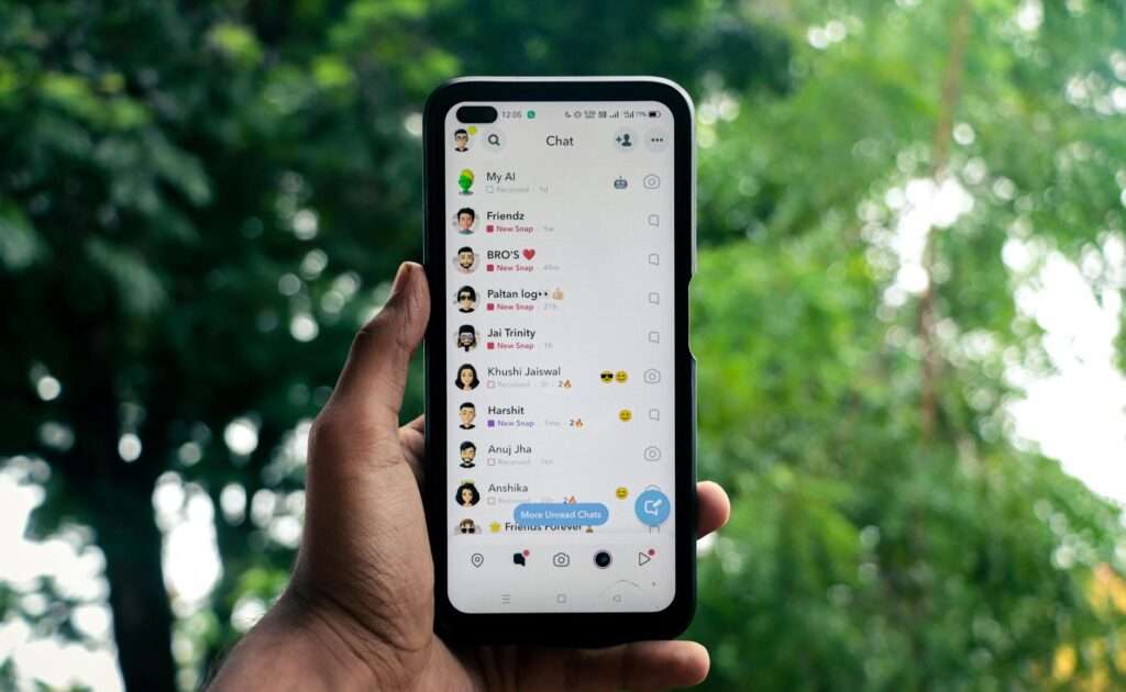 A hand holding a smartphone displaying a chat application outdoors against a green background.