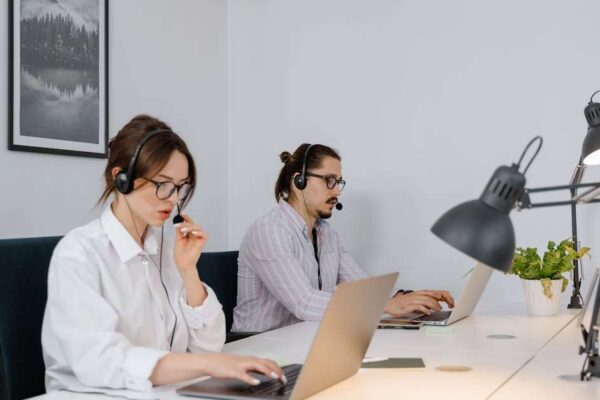 Two call center agents using laptops and headsets in a modern office setting.