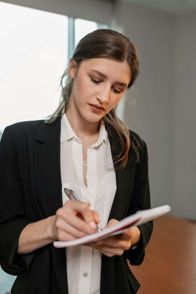 Businesswoman in black blazer concentrating while taking notes in an office.