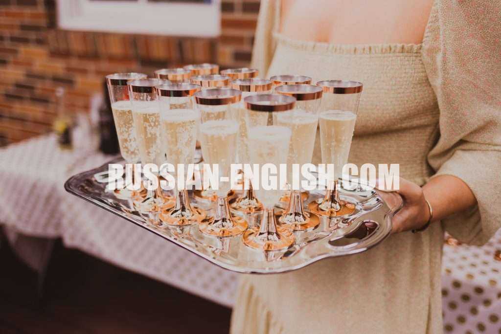 Crop anonymous female in elegant dress holding tray with glasses of champagne in banquet hall